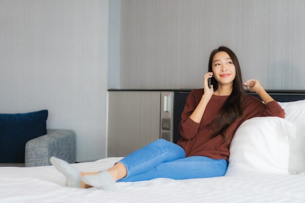 Portrait beautiful young asian woman use smart mobile phone on bed in bedroom interior