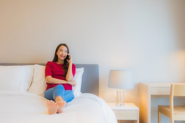 세로 아름 다운 젊은 아시아 여자는 침대에 스마트 휴대 전화를 사용