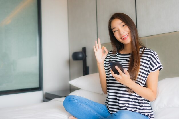 침실에서 초상화 아름 다운 젊은 아시아 여자 사용 스마트 휴대 전화
