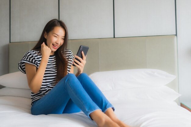 Мобильный телефон пользы женщины портрета красивый молодой азиатский умный в спальне
