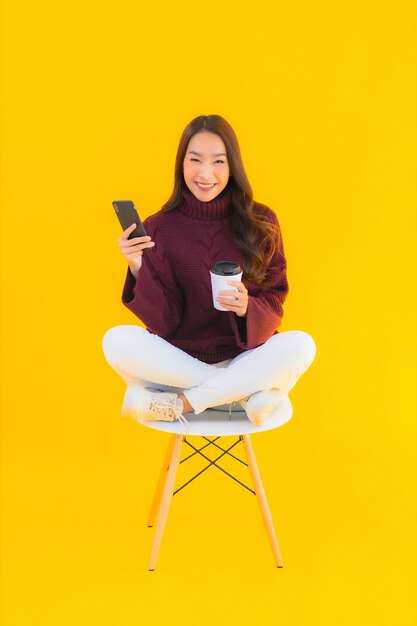 Portrait beautiful young asian woman use smart mobile phone on chair with yellow isolated background