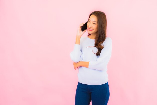 Portrait beautiful young asian woman use smart mobile phone on pink color isolated wall