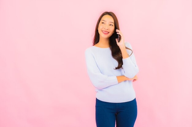 Portrait beautiful young asian woman use smart mobile phone on pink color isolated wall