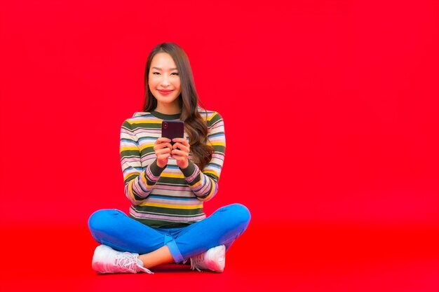 Portrait beautiful young asian woman use smart mobile phone on red isolated wall