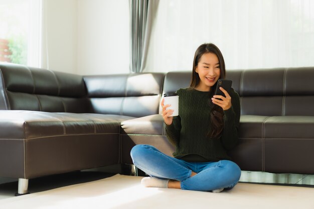 肖像画の美しい若いアジア女性はコーヒーカップとスマートな携帯電話を使用します。