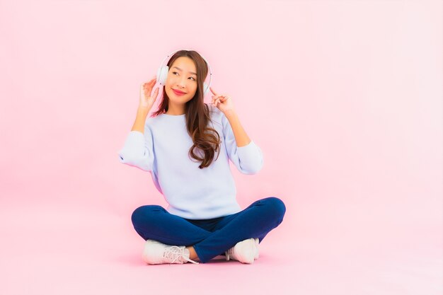 Portrait beautiful young asian woman use smart mobile phone with headphone for listen music on pink wall