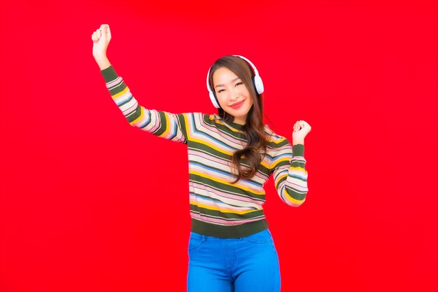 肖像画の美しい若いアジアの女性は、音楽を聴くためにヘッドフォン付きのスマート携帯電話を使用しています