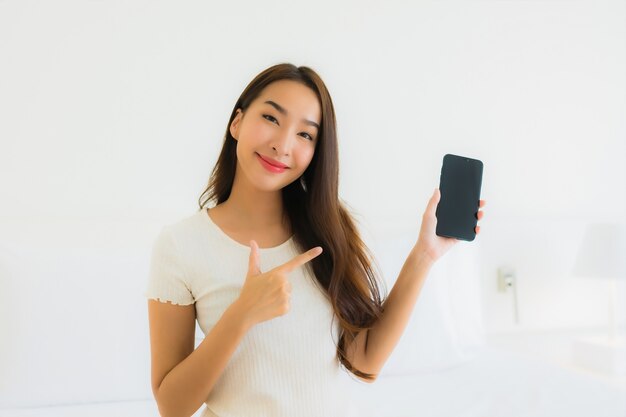 肖像画の美しい若いアジア女性はスマートな携帯電話を使用します