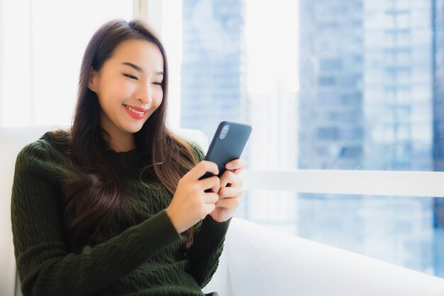 肖像画の美しい若いアジア女性はスマートな携帯電話を使用します