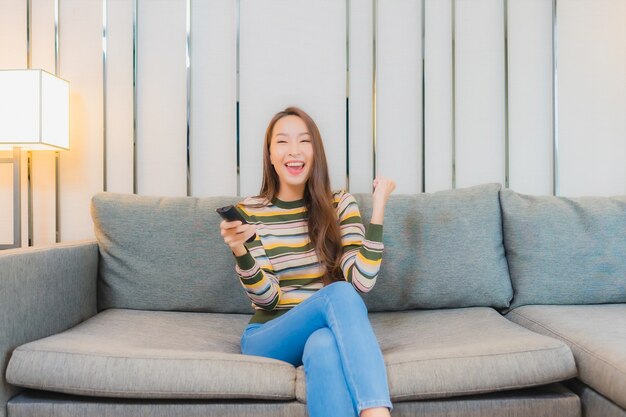 Portrait of beautiful young asian woman use television remote on sofa in living room interior