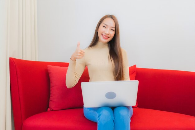 Portrait of beautiful young asian woman uses computer laptop on sofa in living room interior