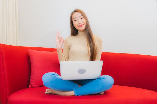 Portrait of beautiful young asian woman uses computer laptop on sofa in living room interior