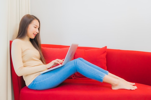 Portrait of beautiful young asian woman uses computer laptop on sofa in living room interior