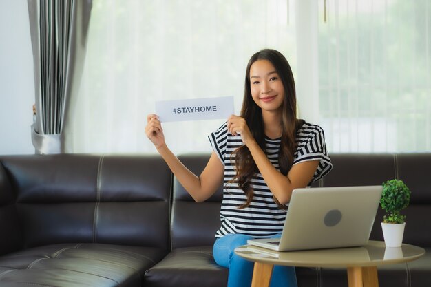 Portrait of beautiful young asian woman using laptop on sofa with stay home paper