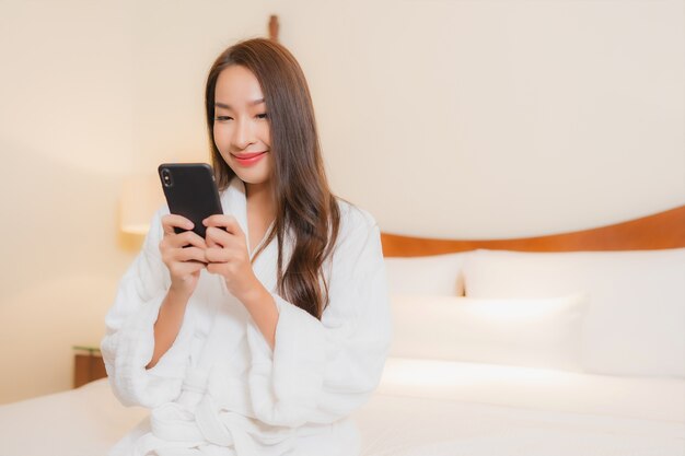 침실 인테리어에 침대에 스마트 휴대 전화를 사용하는 세로 아름다운 젊은 아시아 여자