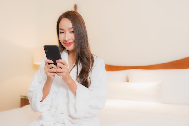 寝室のインテリアのベッドでスマート携帯電話を使用して美しい若いアジアの女性の肖像画