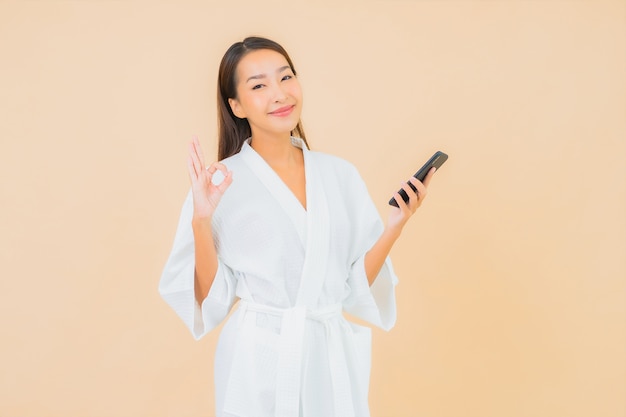 Женщина портрета красивая молодая азиатская используя умный мобильный телефон на бежевом
