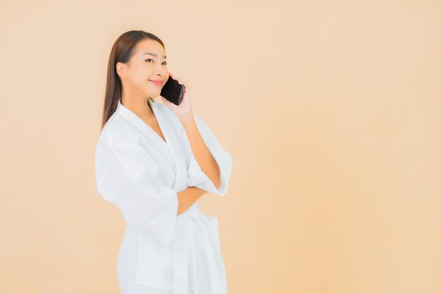 ベージュのスマート携帯電話を使用して美しい若いアジアの女性の肖像画