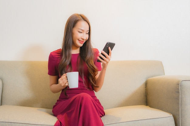 リビングルームのインテリアのソファでスマート携帯電話を使用して美しい若いアジアの女性の肖像画