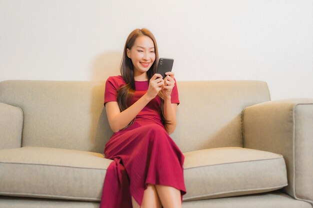 リビングルームのインテリアのソファでスマート携帯電話を使用して美しい若いアジアの女性の肖像画