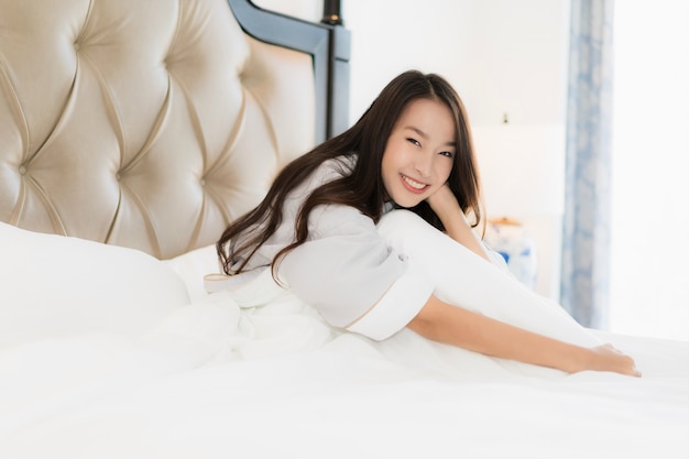 アジアの美しい若い女性の肖像画幸せと目を覚ます、寝室のインテリアのベッドの上の笑顔