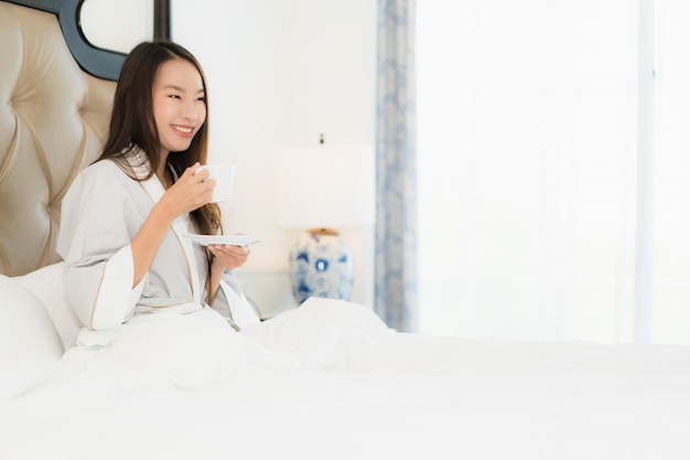 肖像画美しい若いアジア女性の幸せな笑顔と寝室のベッドの上のコーヒーカップで目を覚ます