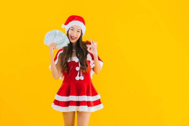 肖像画美しい若いアジアの女性は現金でクリスマスの服と帽子を着用