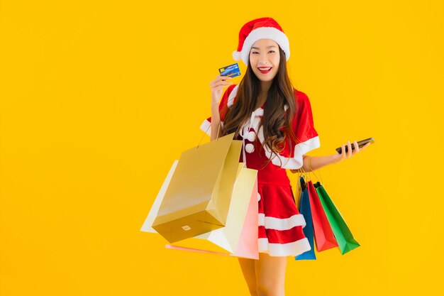 肖像画の美しい若いアジアの女性は多くの買い物袋でクリスマス服の帽子を着用します。