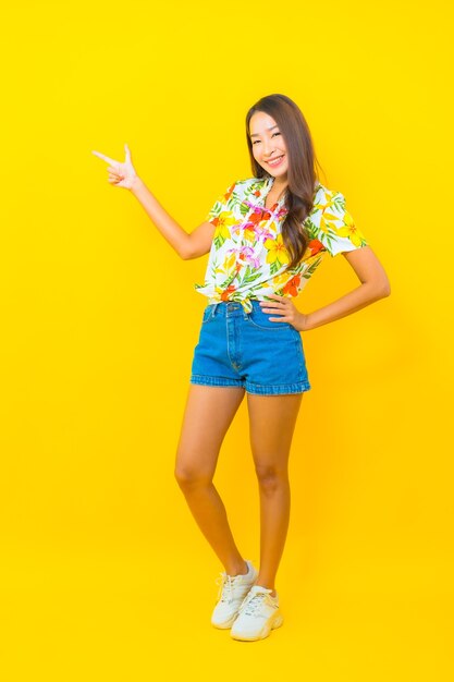 Portrait of beautiful young asian woman wearing colorful shirt and shooting with her finger on yellow wall