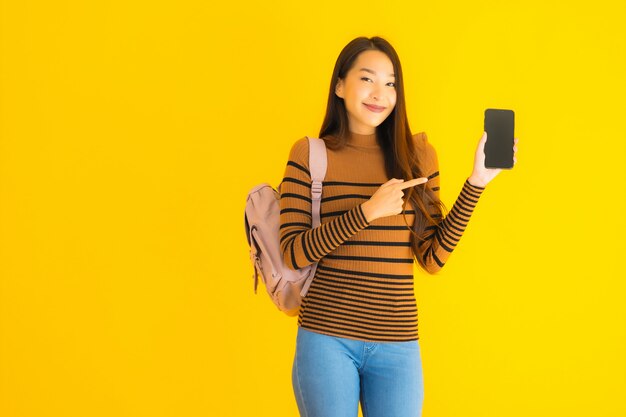 Bagpackで美しい若いアジア女性の肖像画は、スマートフォンを使用しています