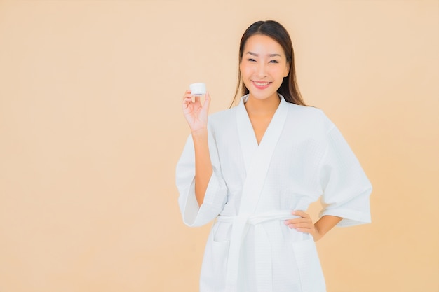 Portrait beautiful young asian woman with bottle lotion and face cream on beige