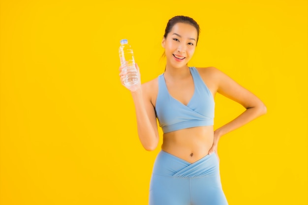 Женщина портрета красивая молодая азиатская с водой бутылки на желтом цвете
