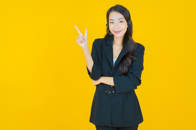 Женщина портрета красивая молодая азиатская с центром обслуживания клиентов центра телефонного обслуживания на желтом желтом цвете