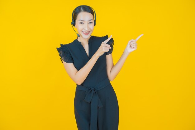 Женщина портрета красивая молодая азиатская с центром обслуживания клиентов центра телефонного обслуживания на желтом цвете