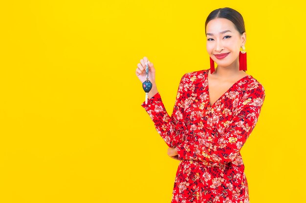 Portrait beautiful young asian woman with car key on yellow wall