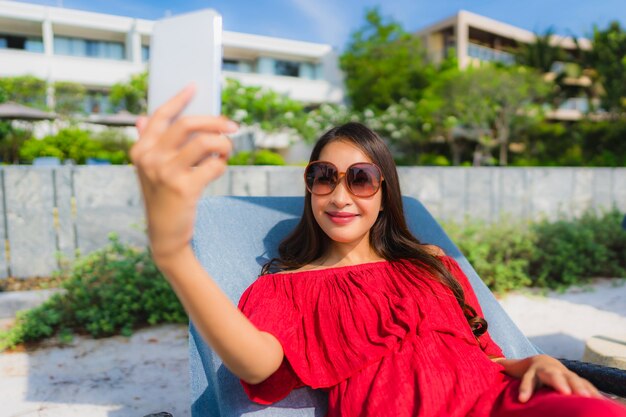 Portrait beautiful young asian woman with cell phone or mobile phone around swimming pool at hotel resort