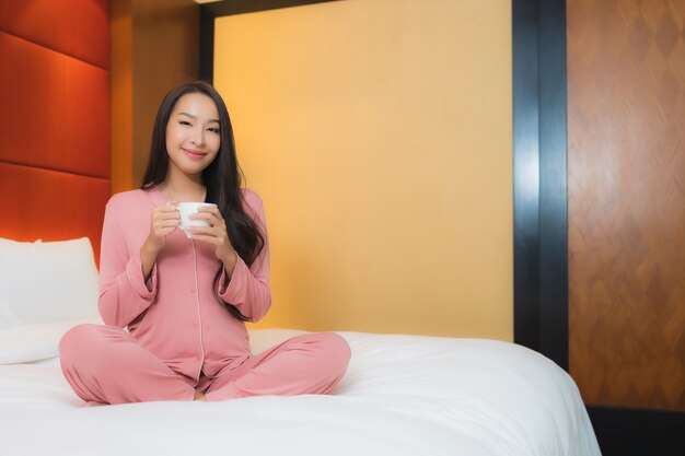 Portrait beautiful young asian woman with coffee cup on bed decoration interior of bedroom