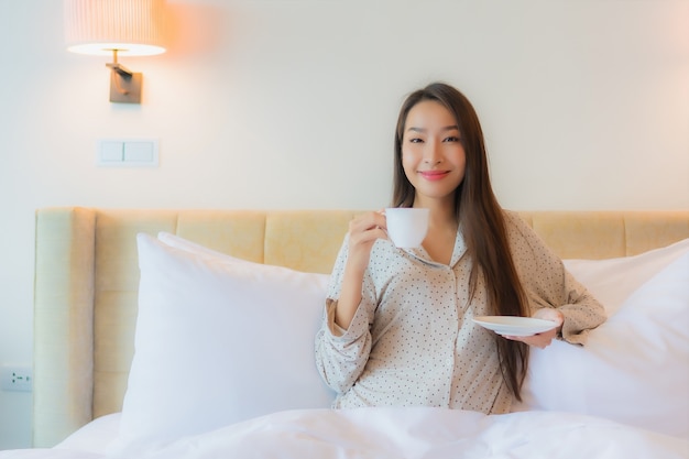 침대에 커피 컵과 세로 아름 다운 젊은 아시아 여자