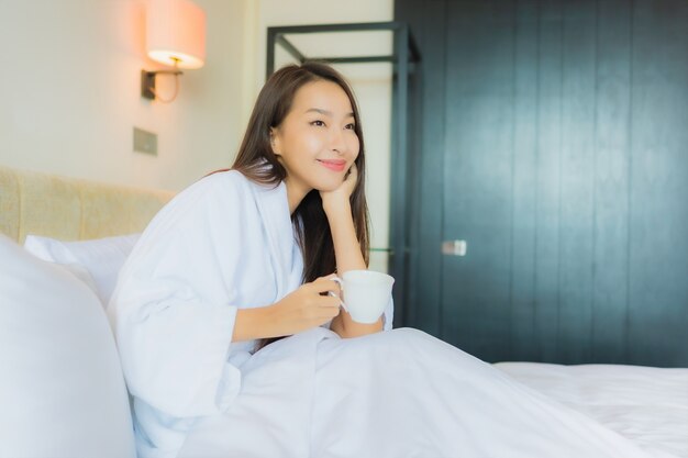 침대에 커피 컵과 세로 아름 다운 젊은 아시아 여자