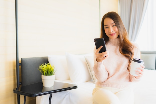 肖像画の美しい若いアジア女性のコーヒーカップとベッドの上の携帯電話
