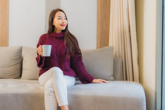 소파 의 장식 인테리어 에 커피 컵 을 들고 있는 아름다운 젊은 아시아 여자 의 초상화