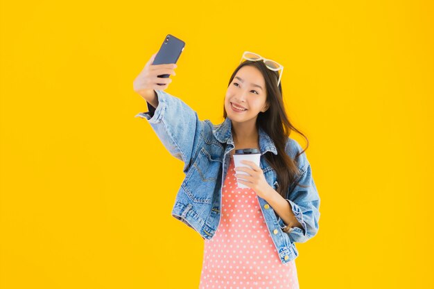 スマートフォンでselfieを取ってコーヒーカップを持つ美しい若いアジア女性の肖像画