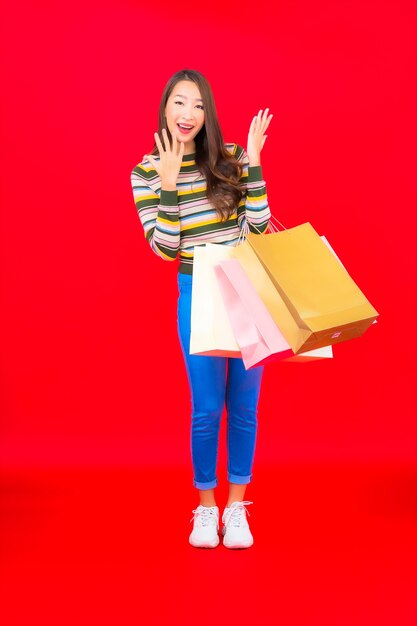 Portrait beautiful young asian woman with colorful shopping bag on red wall