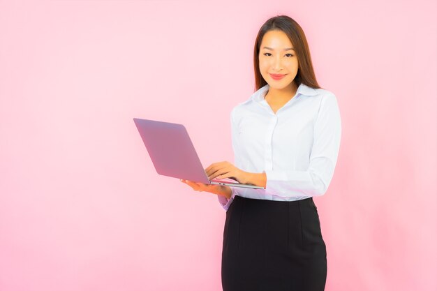 분홍색 벽에 컴퓨터 노트북을 들고 있는 아름다운 젊은 아시아 여성 초상화