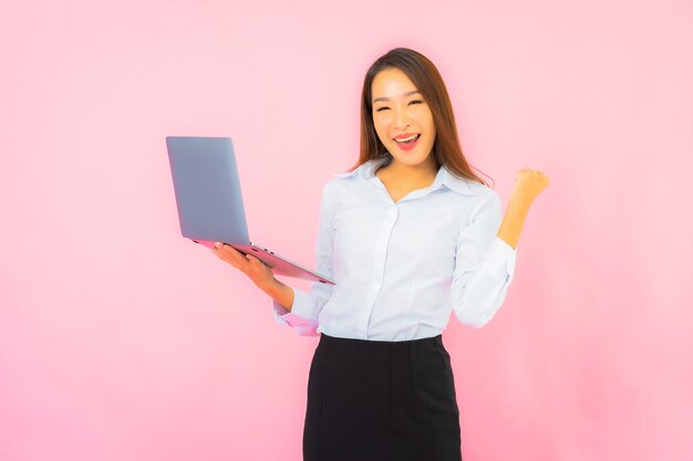 ピンク色の壁にコンピューターのラップトップを持つ肖像画美しい若いアジアの女性