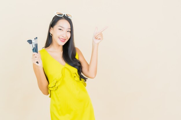 Женщина портрета красивая молодая азиатская с cosmeti составляет щетку на стене цвета