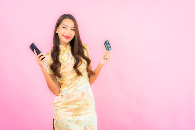 Portrait beautiful young asian woman with credit card and mobile phone on pink color wall