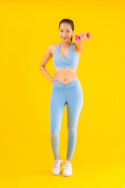 Portrait beautiful young asian woman with dumbbell and sportwear on yellow