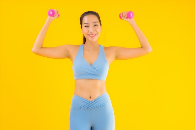 Portrait beautiful young asian woman with dumbbell and sportwear on yellow