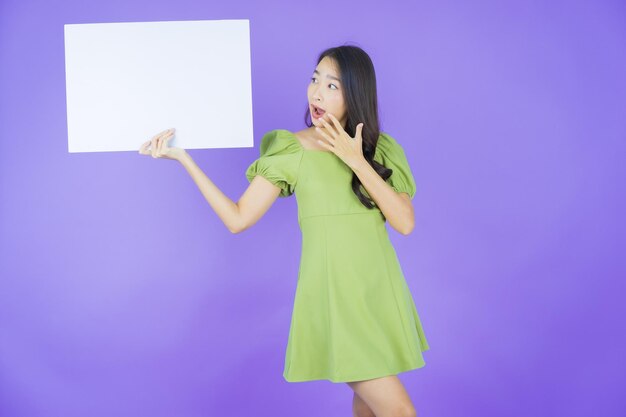 Женщина портрета красивая молодая азиатская с пустым белым рекламным щитом на цветном фоне